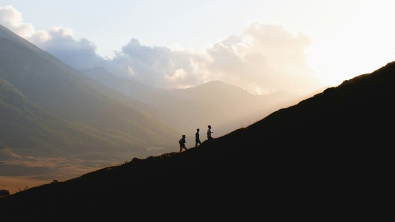 siluetas de tres personas subiendo una montaña