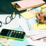 Escritorio con papeles, calculadora, anteojos y mano con birome