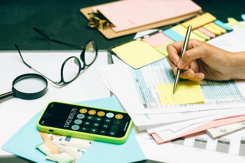 Escritorio con papeles, calculadora, anteojos y mano con birome